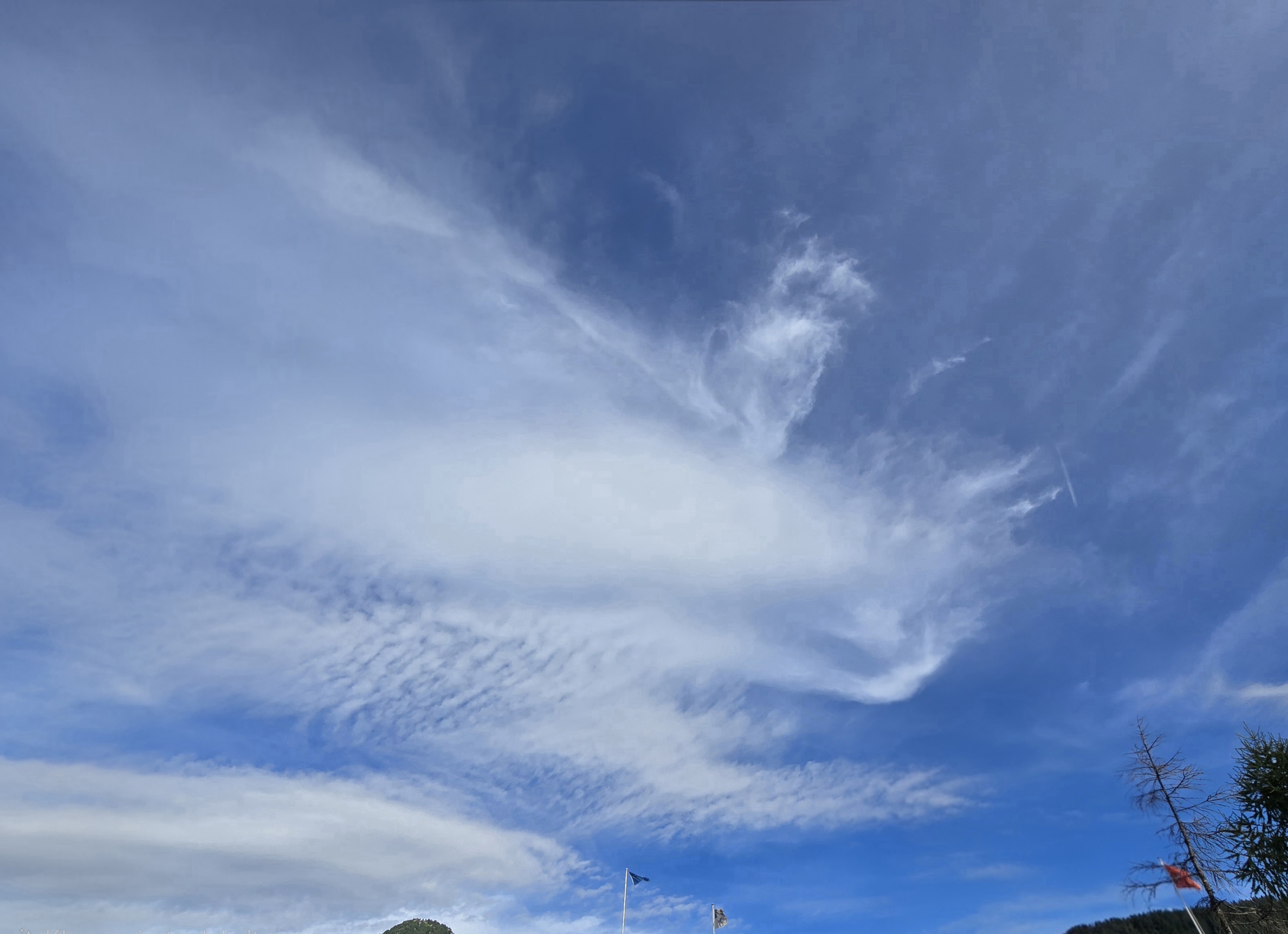 Helle, teils linsenförmige Wolken mit faserigen Rändern und feinen Wolkenreihen vor blauem Himmel