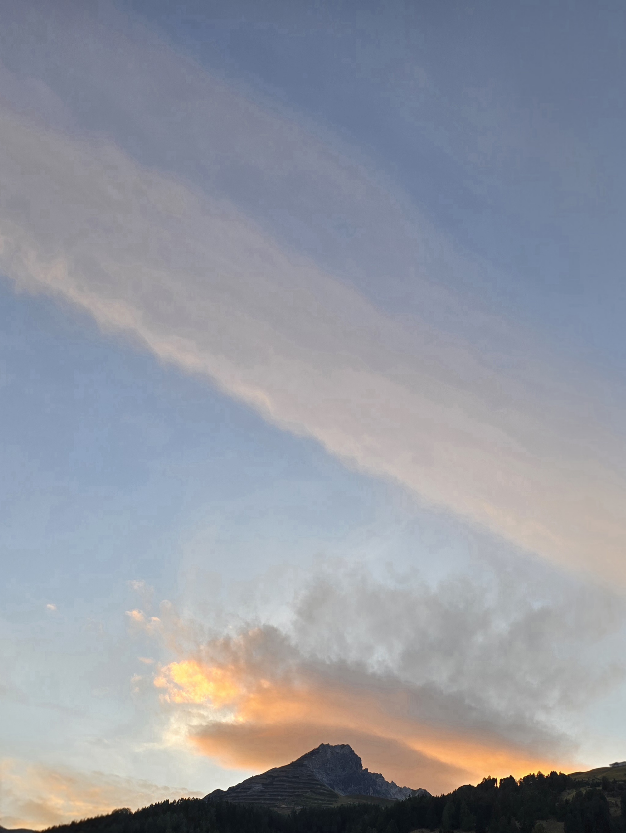 Breites blasses Wolkenband über einer orange beleuchteten Wolke an der Bergsilhouette
