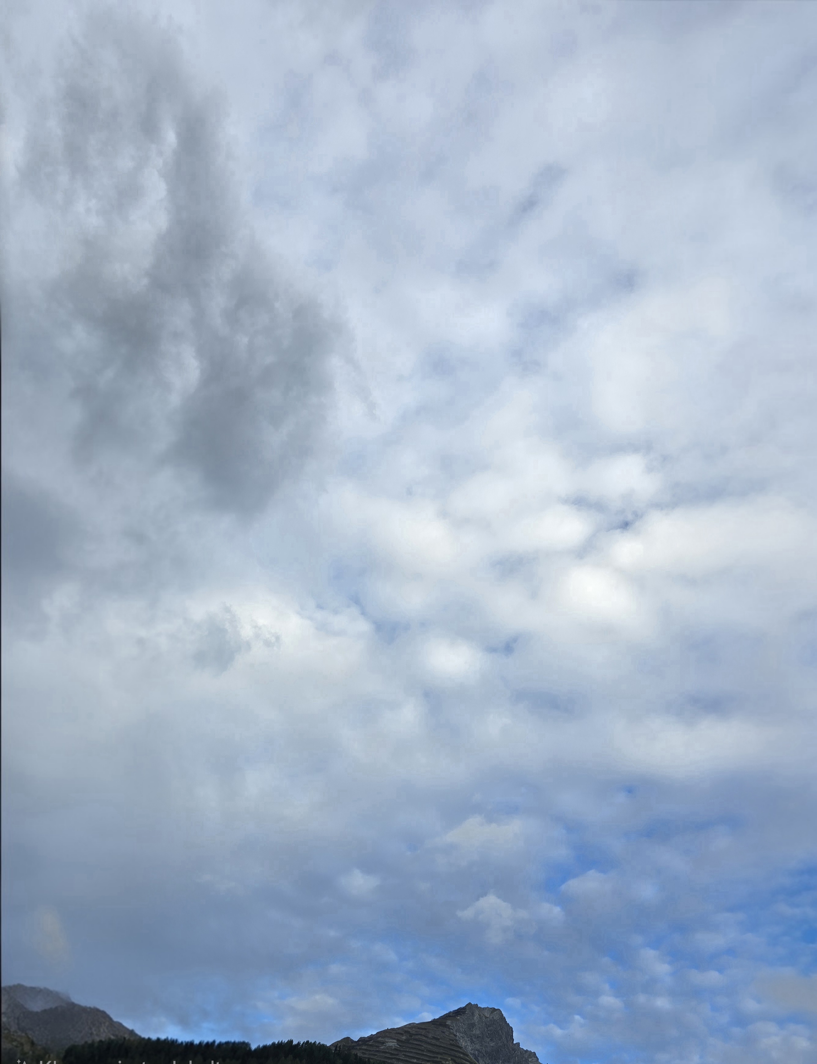 Graue und weisse Wolken bedecken weite Teile des Himmels. Über dem Berg öffnet sich ein blauer Streifen.